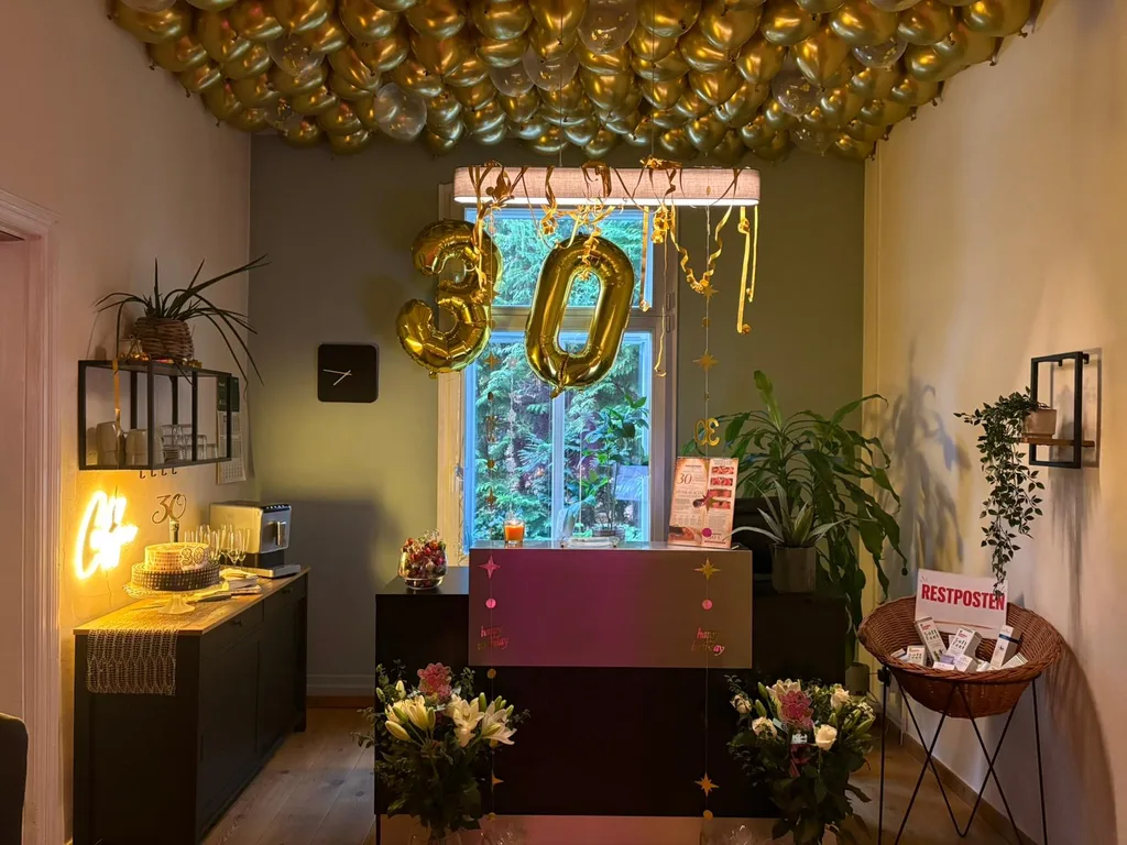 Festlich geschmückter Empfang des Physiotrom-Studios: eine Decke voller goldener Luftballons, eine große 30 aus Luftballons vor dem Fenster, dazu Blumen, Torte und Sektgläser.