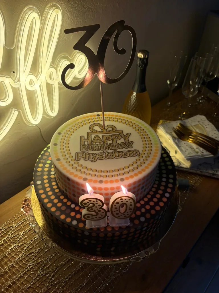 Zweistöckige Jubiläumstorte mit der Aufschrift „Happy Birthday Physiotrom“, brennenden 30er-Kerzen und einem goldenen 30-Cake-Topper, daneben Sektflasche und Gläser.
